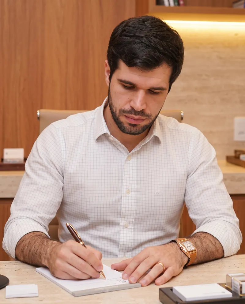 Dr. José Ricardo Ristow fazendo anotações num bloco, sentado à mesa do consultório
