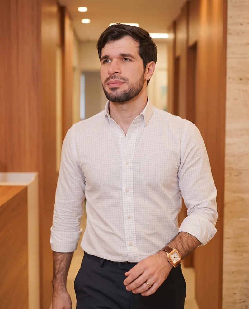 Dr. José Ricardo Ristow caminhando pelo corredor do consultório, de camisa clara e calça escura