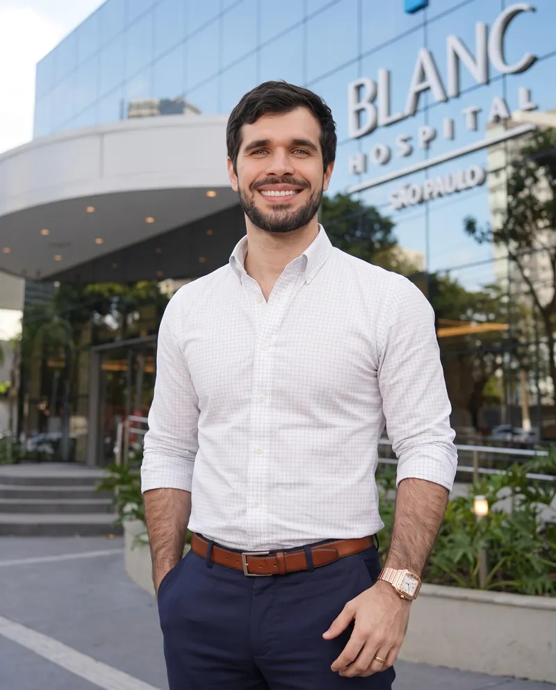 Dr. José Ricardo Ristow sorrindo em frente à fachada do Blanc Hospital, com o letreiro do hospital ao fundo