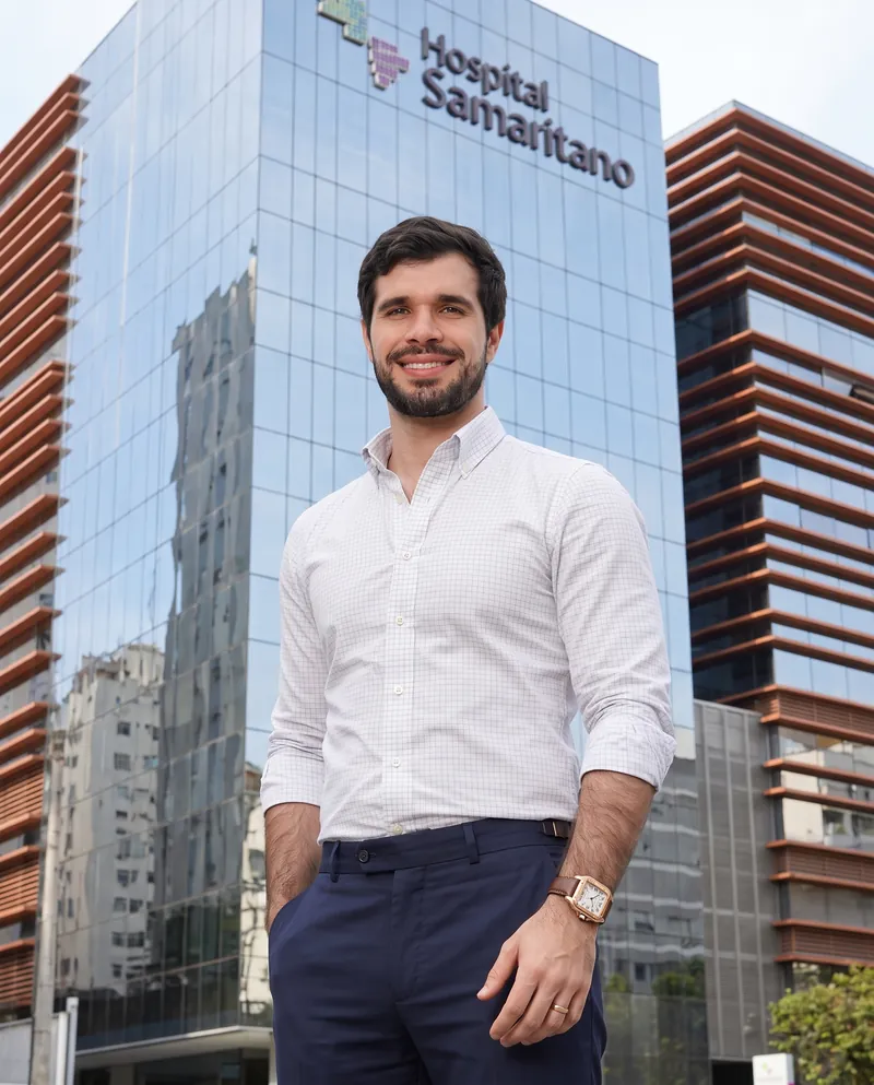 Dr. José Ricardo Ristow sorrindo em frente à fachada do Hospital Samaritano Paulista, com o letreiro do hospital ao fundo