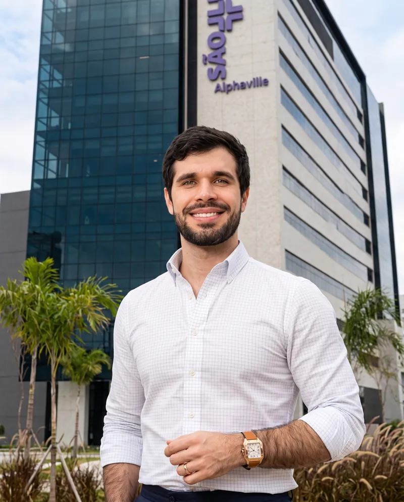 Dr. José Ricardo Ristow sorrindo em frente à fachada do Hospital São Luiz Alphaville, com o letreiro do hospital ao fundo